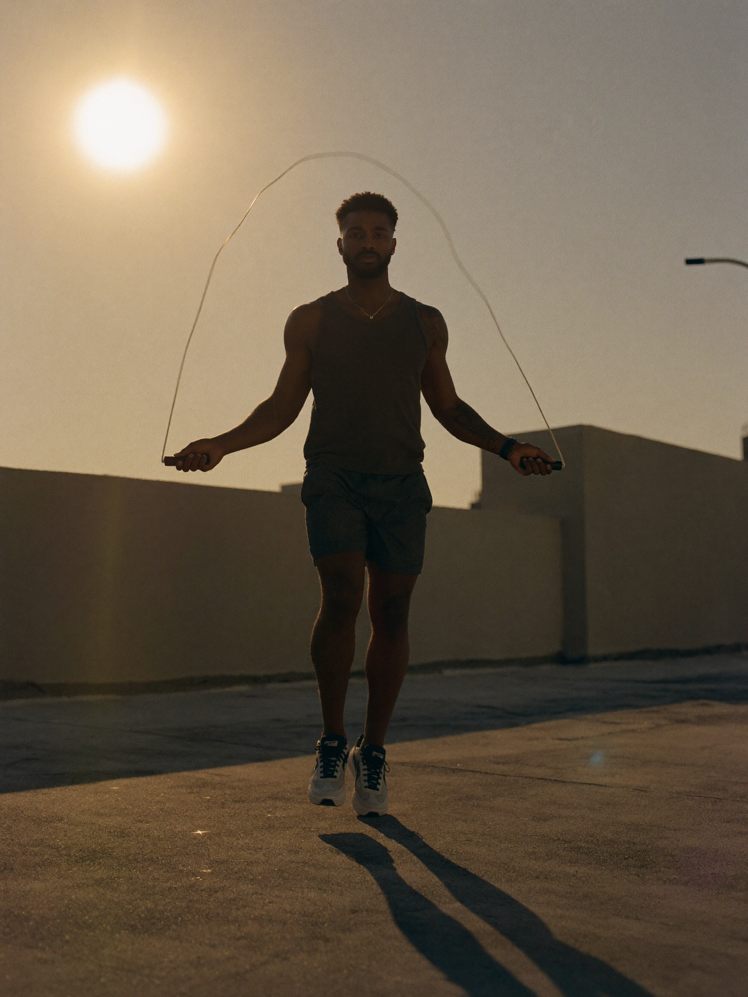 A person jumping rope mid-air on a rooftop at golden hour, the rope arcing overhead against the setting sun.